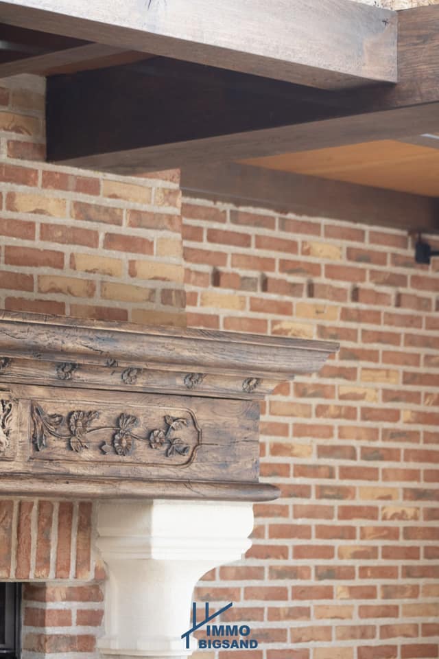 Houten schouwbalk met snijwerk tegen een bakstenen muur
