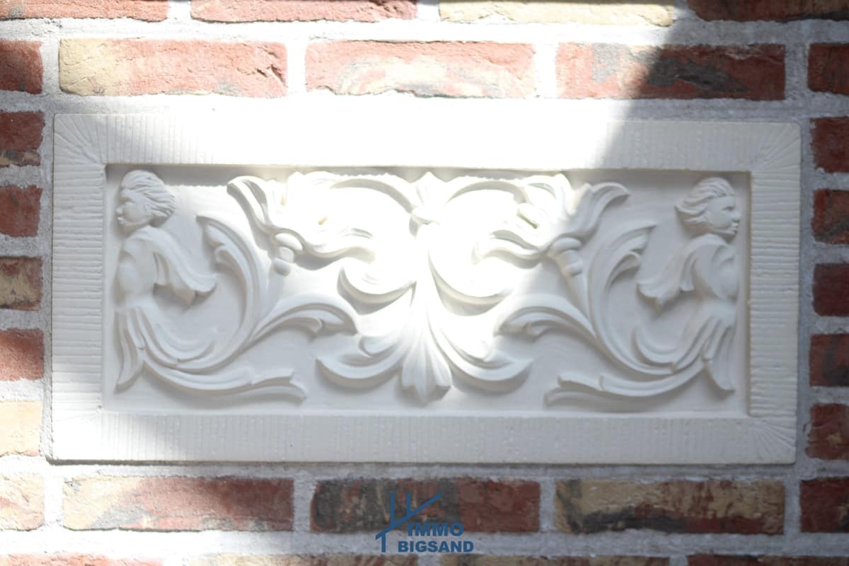 Wit reliëf met figuren en bladwerk in een bakstenen muur